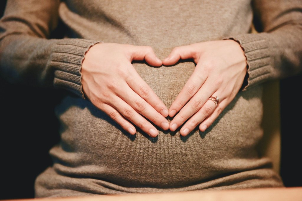 Hände in Herzform auf einem Schwangerschaftsbauch liegend